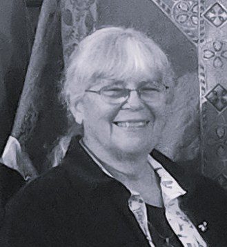 Smiling woman with glasses and white hair.