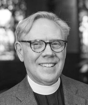 Smiling man with glasses and clerical collar.