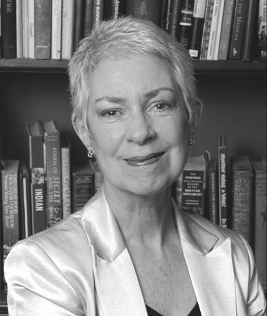 Woman with short gray hair smiling by bookshelf