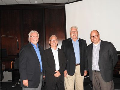 Four men in suits smiling indoors