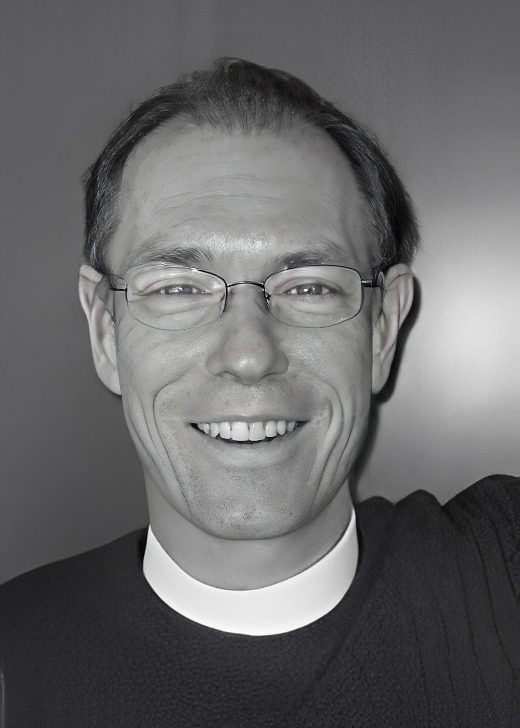 Smiling man in clerical collar and glasses