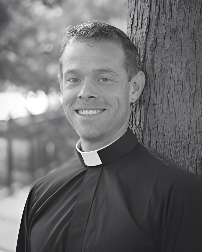 Smiling man wearing clerical collar by tree